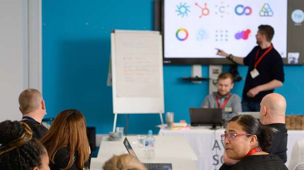 Our creative director Tom Walton pointing at a screen of company logos in front of an audience during a workshop